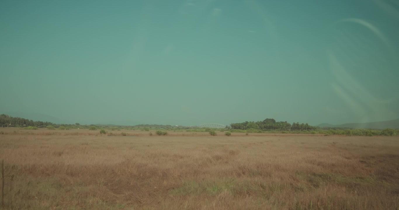 Uitzicht vanuit een rijdend voertuig met een droog, open landschap dat voorbijtrekt onder een heldere hemel