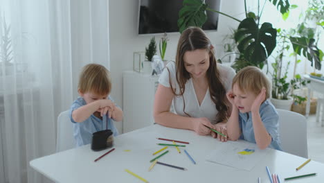 Mutter-Und-Ihre-Beiden-Söhne-Sitzen-Am-Küchentisch-Und-Zeichnen-Buntstifte.-Familienzeichnung-Auf-Dem-Rasen-Im-Sommer.-Jungen-Lernen-Zeichnen-Und-Mama-Hilft-Beim-Zeichnen