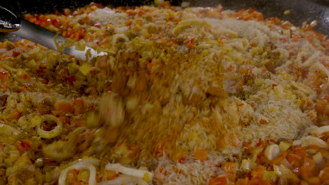 vista sobre un plato de pealla donde se acaba de agregar el arroz fresco y está listo para revolver