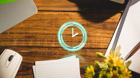 Animation-of-clock-ticking-over-notebook-and-laptop-on-wooden-table