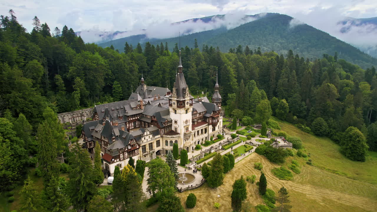 Luftdrone-utsikt over Peleș slott i Romania. Slott med hager og turister i Karpatene, frodig skog rundt.
