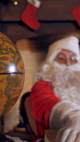 santa looking at the globe. santa claus is sitting and turning the model of the globe. envelope in santa's hands. christmas time. vertical video