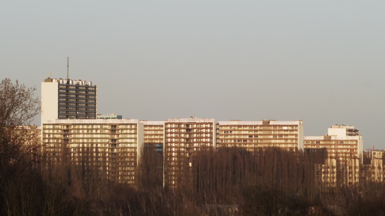 Wide-angle view of high-rise residential buildings in Linkeroever, Antwerp, with bare trees and warm spring sunset light