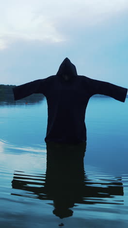 Evil witch in black cloak with hood in the river. Halloween costume.. Vertical video