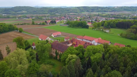 a drone moves forward, kalsdorf castle, green fields and trees under cloudy skies