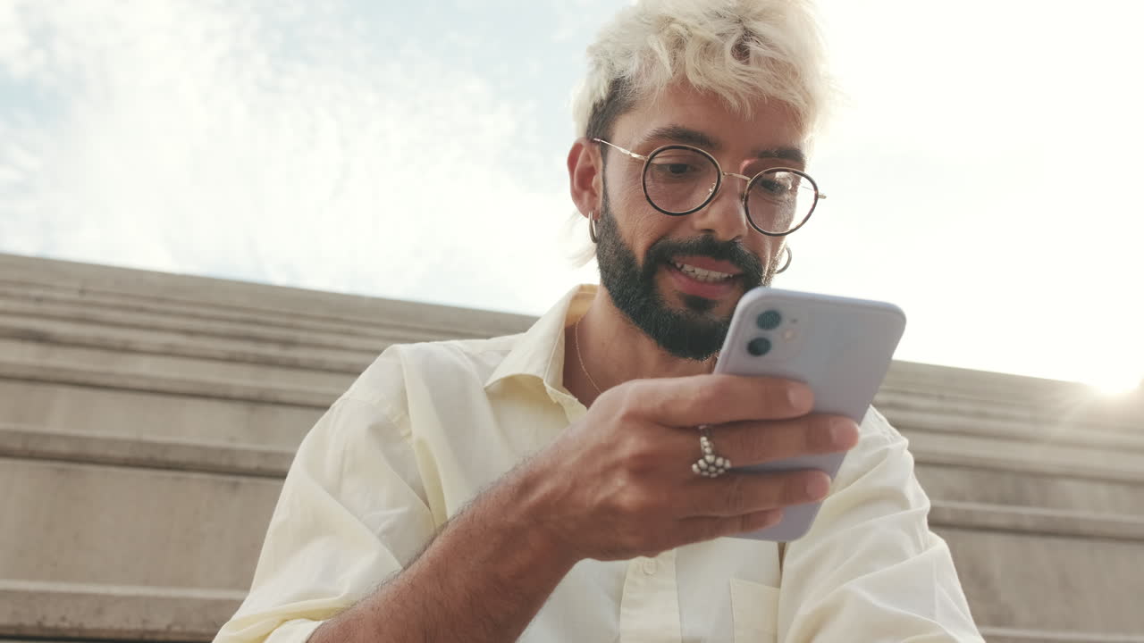 Giovane con capelli decolorati che usa lo smartphone all'aperto