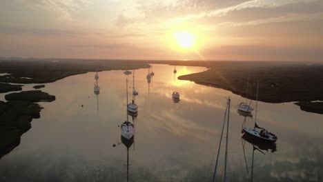 Toma-De-Un-Dron-Bajo-De-Un-Hermoso-Amanecer-Sobre-Aguas-Tranquilas-Con-Reflejos-Y-Veleros-Y-Marismas-Y-Arroyos-En-Pozos-Al-Lado-Del-Mar-Norte-De-Norfolk,-Costa-Este-Del-Reino-Unido