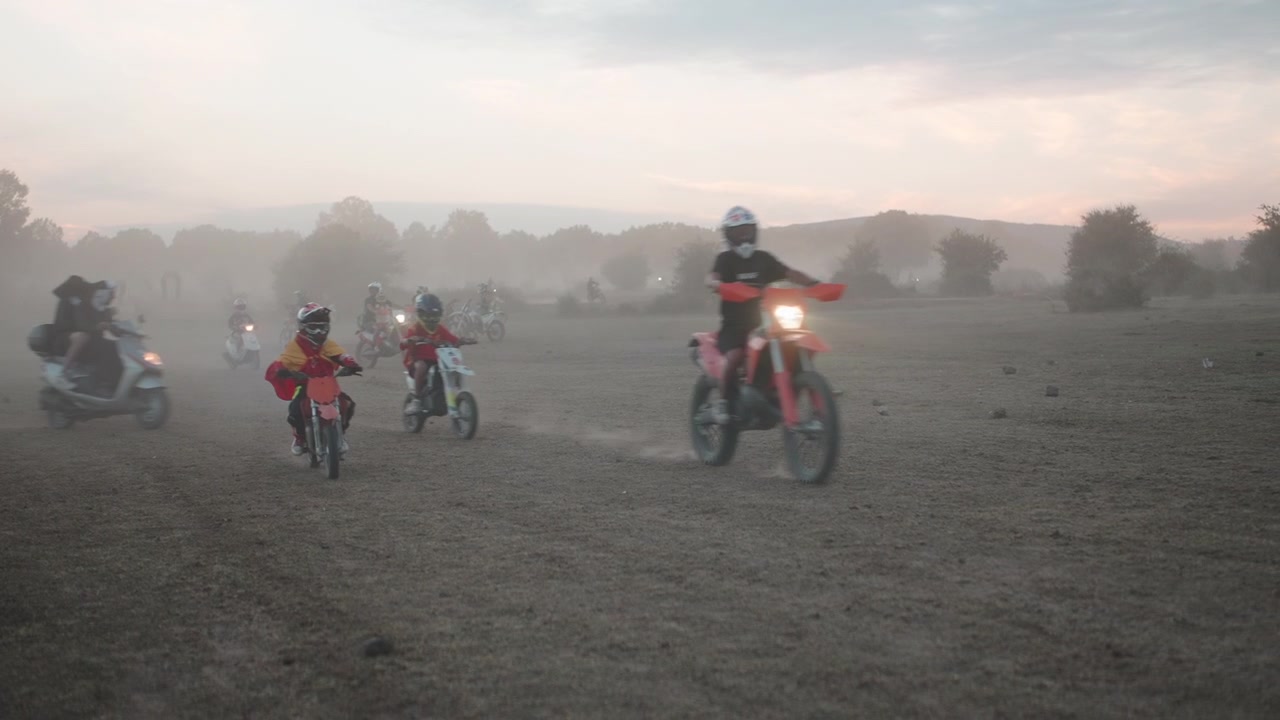 Grupo de Motociclistas Atravessando Campo Poeirento ao Pôr do Sol