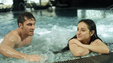 beautiful couple meeting in spa pool. guy and girl relaxing in whirlpool inside