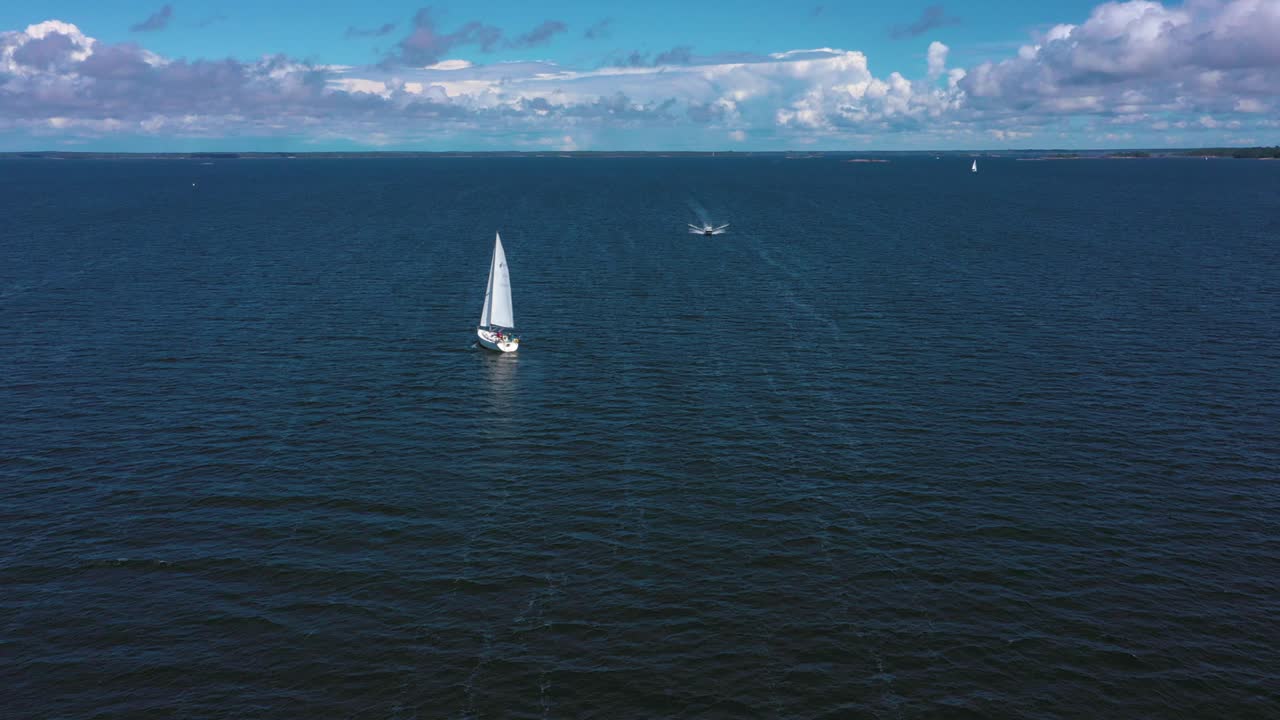 Aerial view of a boat approaching a white sailboat on the open sea, on the Gulf of Finland, on a sunny, summer day, near Hanko, in Uusimaa, Finland - tracking, drone shot