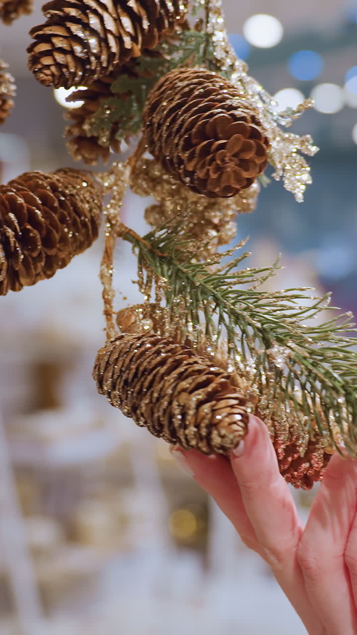 Close-up of lady gently holding a decorated pinecone garland in a decor shop, the festive and shimmering decor creates a cozy, warm atmosphere