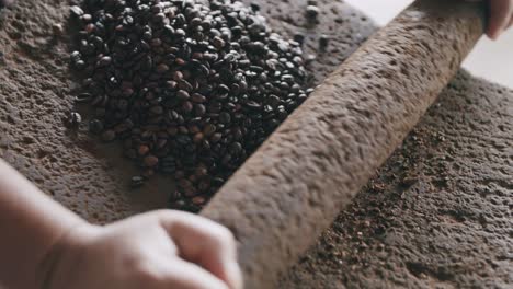 imágenes en cámara lenta de una persona que empieza a moler granos de café en una piedra volcánica con un pasador de piedra