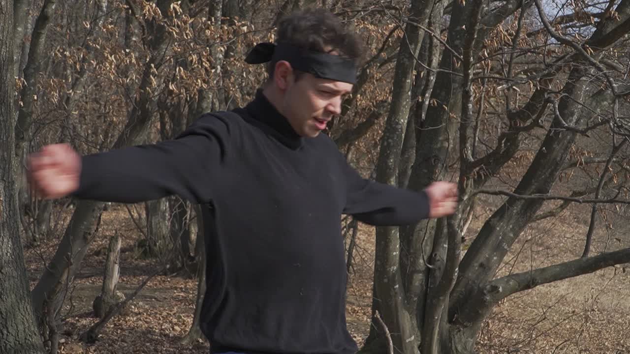 A ninja in black attire stretches his arms during a warm-up session in a forest setting. Perfect for themes of martial arts, training, discipline, and combat preparation