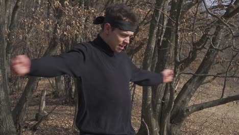 A ninja in black attire stretches his arms during a warm-up session in a forest setting. Perfect for themes of martial arts, training, discipline, and combat preparation