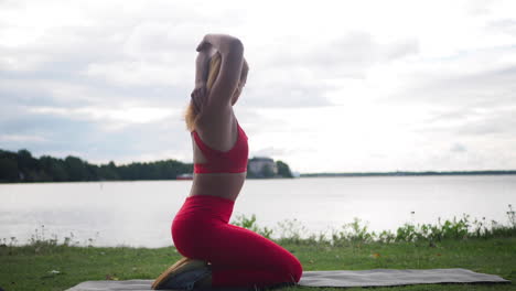 young woman in red sportswear sitting on yoga mat outside doing exercises and practicing yoga