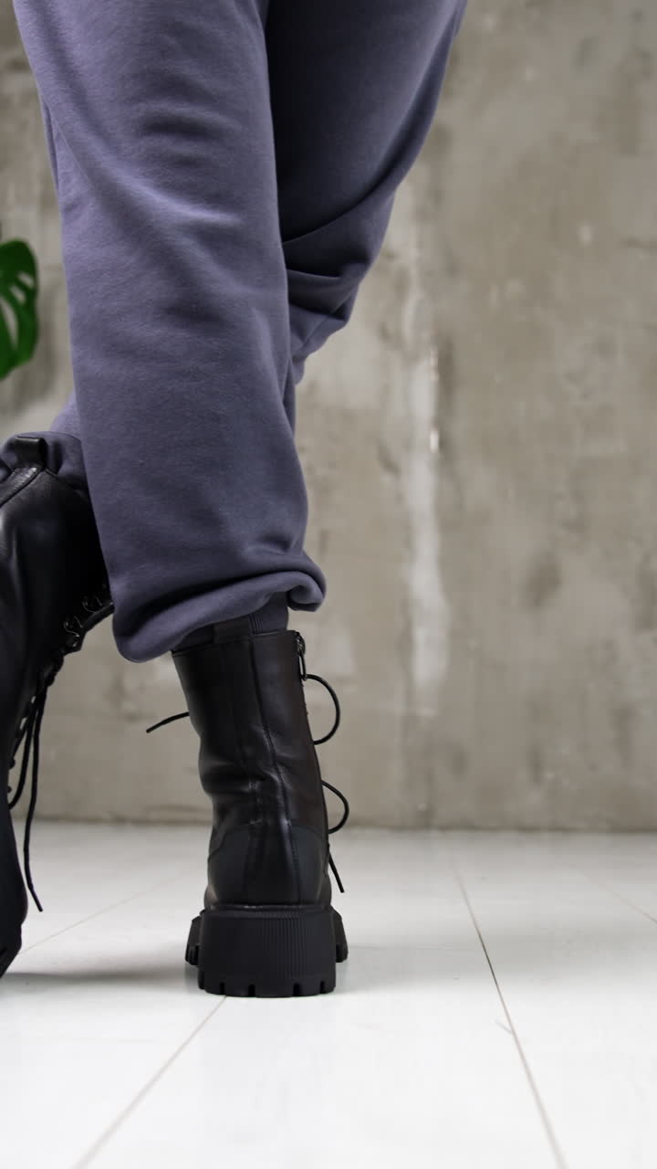 Female model standing her back to camera in black tractor boots. Woman demonstrating the modern stylish footwear in studio. Vertical video