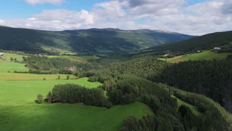 Aerial-view-of-a-beautiful-green-valley-surrounded-by-mountains-on-a-sunny-day-with-some-clouds