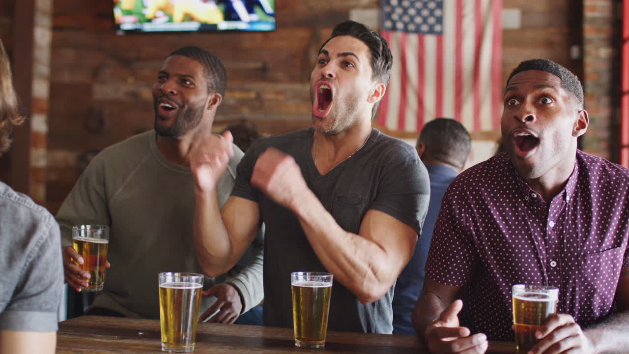 grupo de amigos masculinos celebrando mientras ven el juego en la pantalla en un bar deportivo