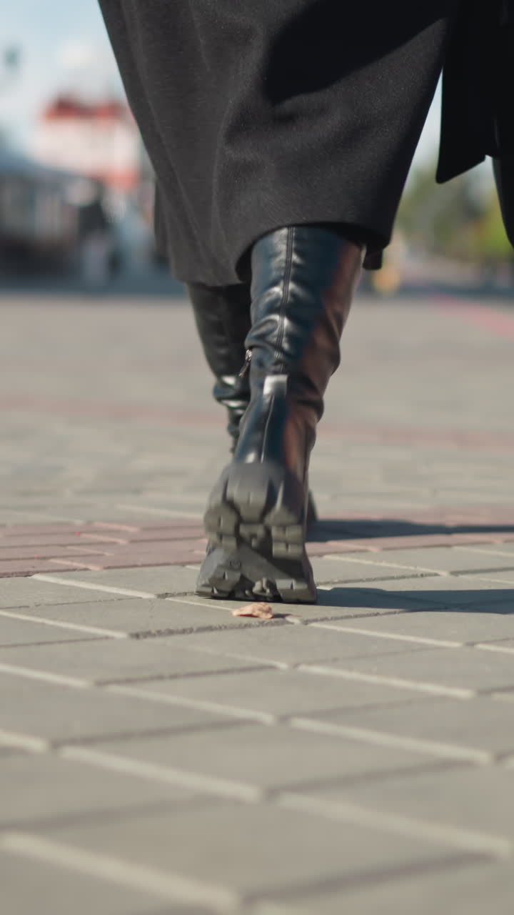 vista de la pierna de una dama con botas negras y abrigo sosteniendo un maletín negro paseando por un camino entrelazado en un entorno urbano, que representa un paso listo para el negocio