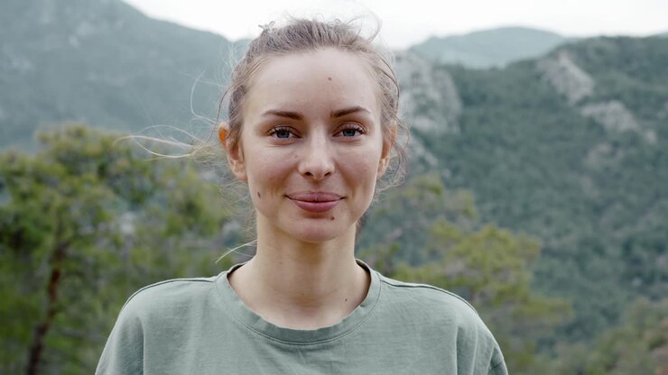 Portrait of beautiful woman standing in front camera - high green hills on background