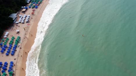 Hermosa-Vista-Aérea-De-Drones-A-Vista-De-Pájaro-De-La-Playa-Tropical-Praia-Do-Madeiro-Con-Coloridas-Sombrillas-De-Playa-Y-Turistas-Nadando-Y-Surfeando-Cerca-De-La-Famosa-Ciudad-De-Pipa-En-El-Norte-De-Brasil