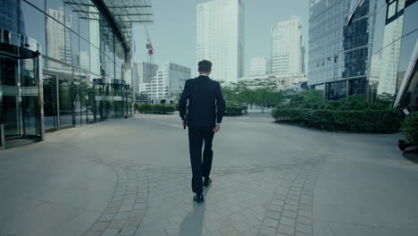 Back-view-of-a-man-in-suit-walking-outside-office-building-with-his-laptop-returning-home-during-evening-time