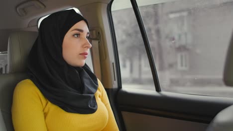 young muslim woman in hijab sitting in car on passenger rear seat. muslim woman day dreaming in back seat. a young woman in a hijab looks out the window.