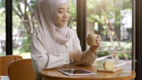 Una-Mujer-Musulmana-Asiática-Con-Movilidad-Ascendente-Que-Disfruta-De-Un-Momento-Relajante-En-La-Cafetería-En-Un-Día-Soleado