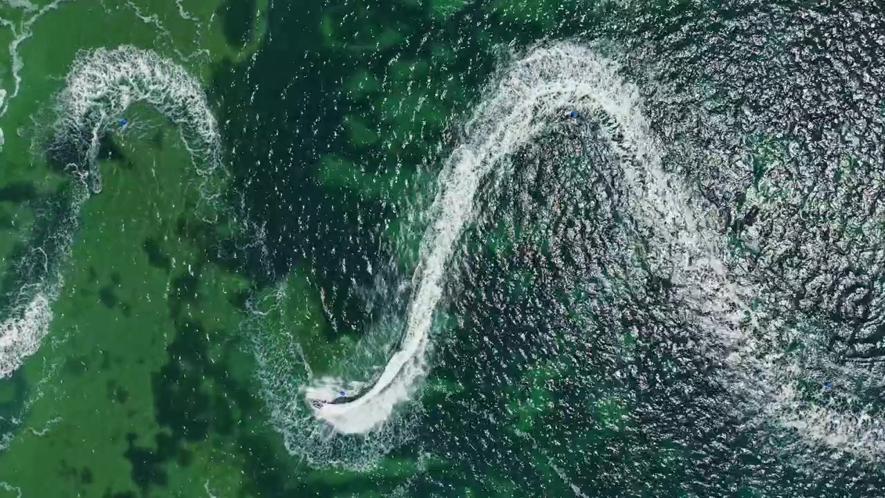 Jetski-ræs finder sted på en solrig dag i åbent vand, hvor kørere konkurrerer i højthastighedsmanøvrer og skaber bølger nær kysten.