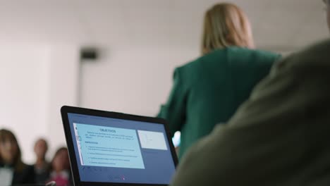 hombre usando un cuaderno mientras una mujer de atrás da clases a un grupo de personas