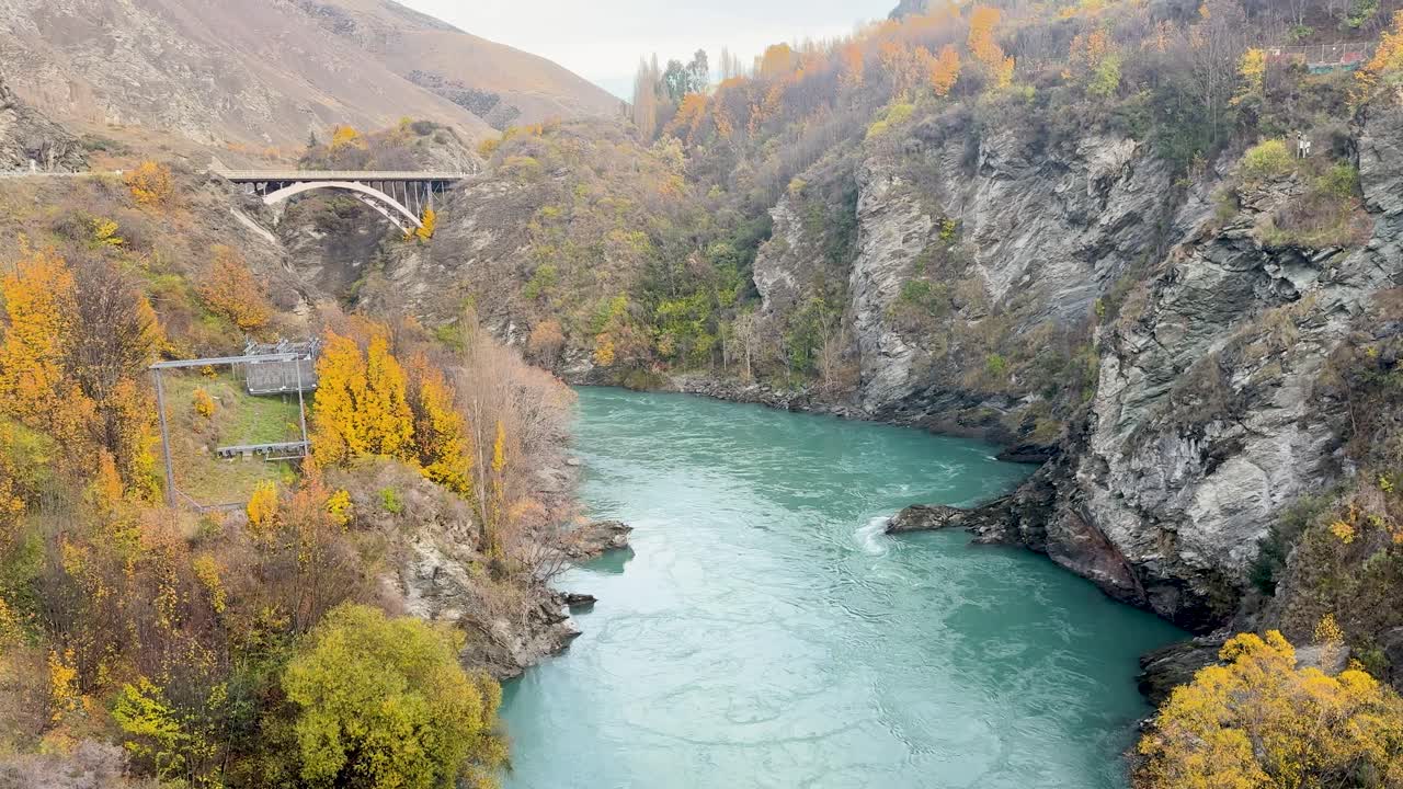A serene autumn landscape with a turquoise river flowing under a bridge in Queenstown, New Zealand