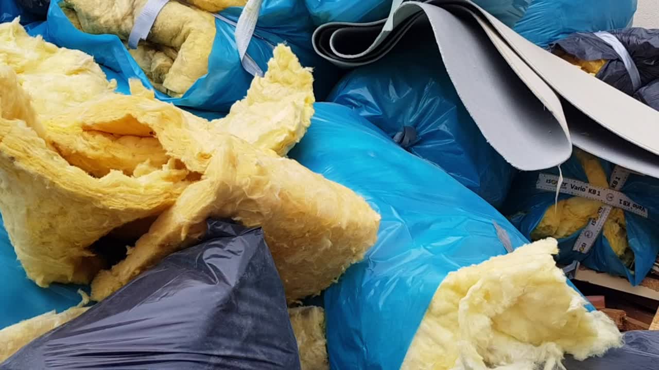 건설 현장에서 파란색 플라스틱 쓰레기 봉투에 있는 벽 유리 섬유 단열 시트를 아래로 패닝