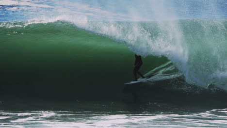 Surfer exits clean barreling wave framed by powerful green face and foamy trail