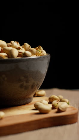 video vertical de primer plano de estudio de un cuenco de nueces de pistacho en conchas girando contra un fondo de estudio negro