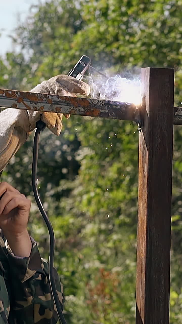 slow motion skilled craftsman in protective mask welds metal rail of new fence with modern tool on day