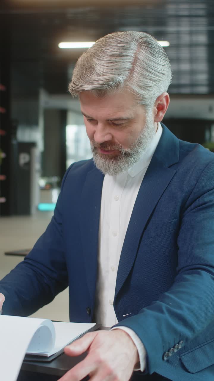 Happy caucasian mature male entrepreneur in suit analyzing graph documents reports in office lobby