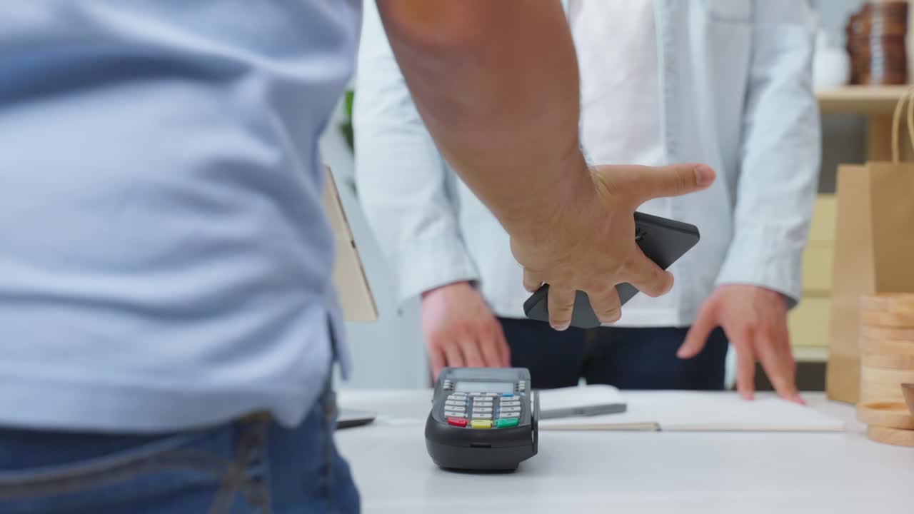 mãos próximas de jovem usar telefone móvel pagar para a encomenda de mercadorias de vaso. cliente masculino atraente bonito fazendo um pagamento sem contato fácil e rápido para o produto de pequena empresa na loja de armazém.