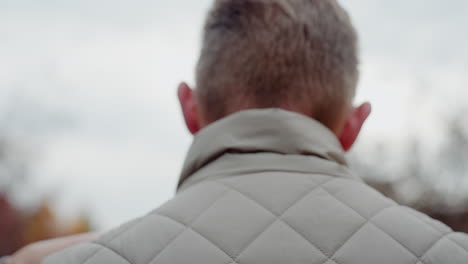 back view of man in summer jacket being embraced by woman with pink painted nails resting hands on his shoulders as they share intimate hug outdoors under soft daylight with affection and connection