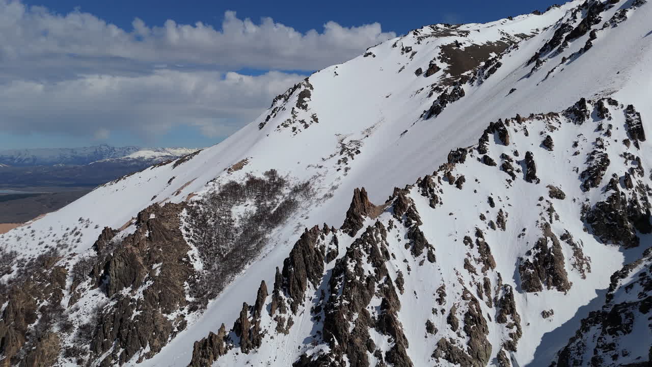 Slow daisy cutter drone shot over uncharted backcountry cliff section in La Hoya ski resort in Esquel, Argentina. 4K-60fps