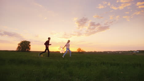 a man and a woman have fun - running around the field at sunset with balloons