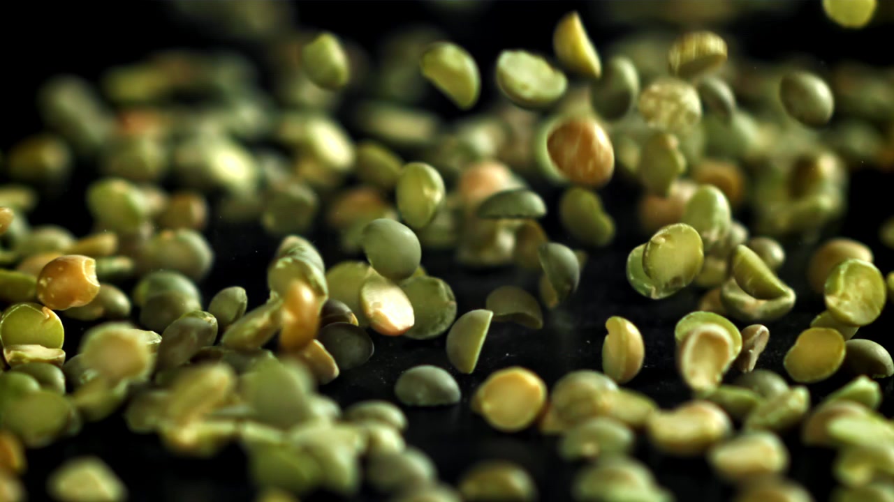 Split Green Peas Falling onto Black Surface in Slow Motion