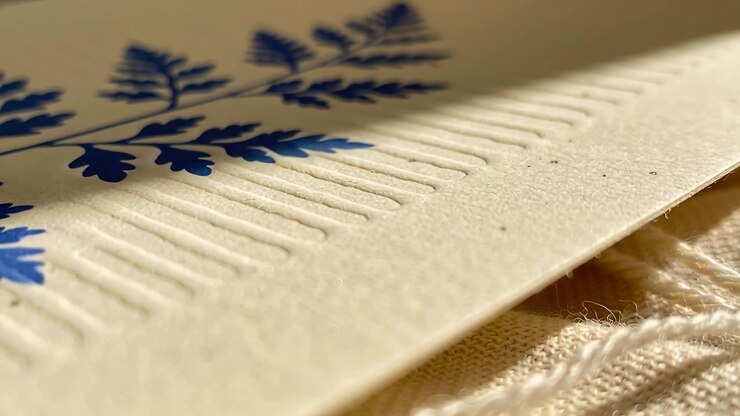 Pulling focus, lens revealing cream card, fern print and embossing on woven cloth, showing texture