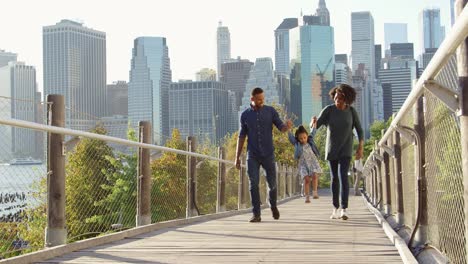 black couple and daughter walking on footbridge in manhattan