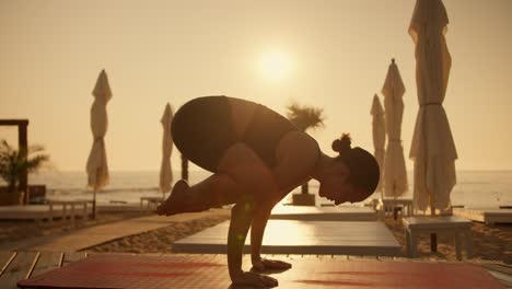 A-brunette-girl-in-a-summer-sports-uniform-does-yoga-and-gets-into-a-bird-pose-on-a-red-mat-on-a-sunny-beach-in-the-summer