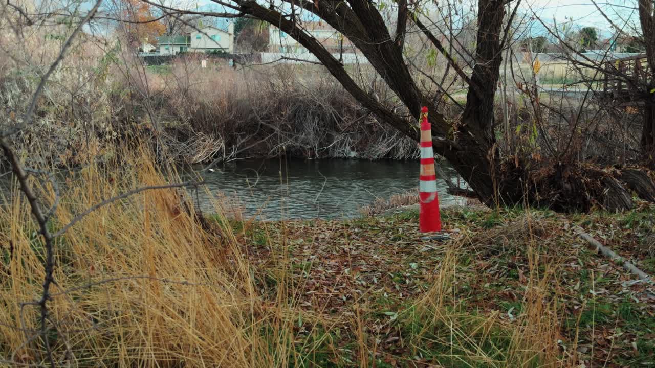 Slow motion pan reveals river water flowing under a bridge with an orange traffic cone nearby