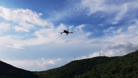 orbit around silhouette of quad copter drone flying against cloudy sky and mountainous region background