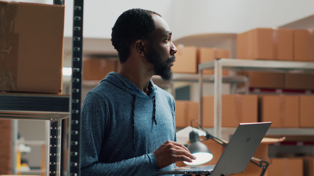 Man using laptop in warehouse surrounded by boxes