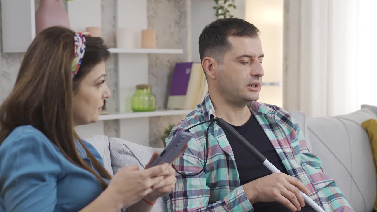 그의 아내는 휴대폰을 보면서 맹인이 궁금해하는 것을 말합니다.