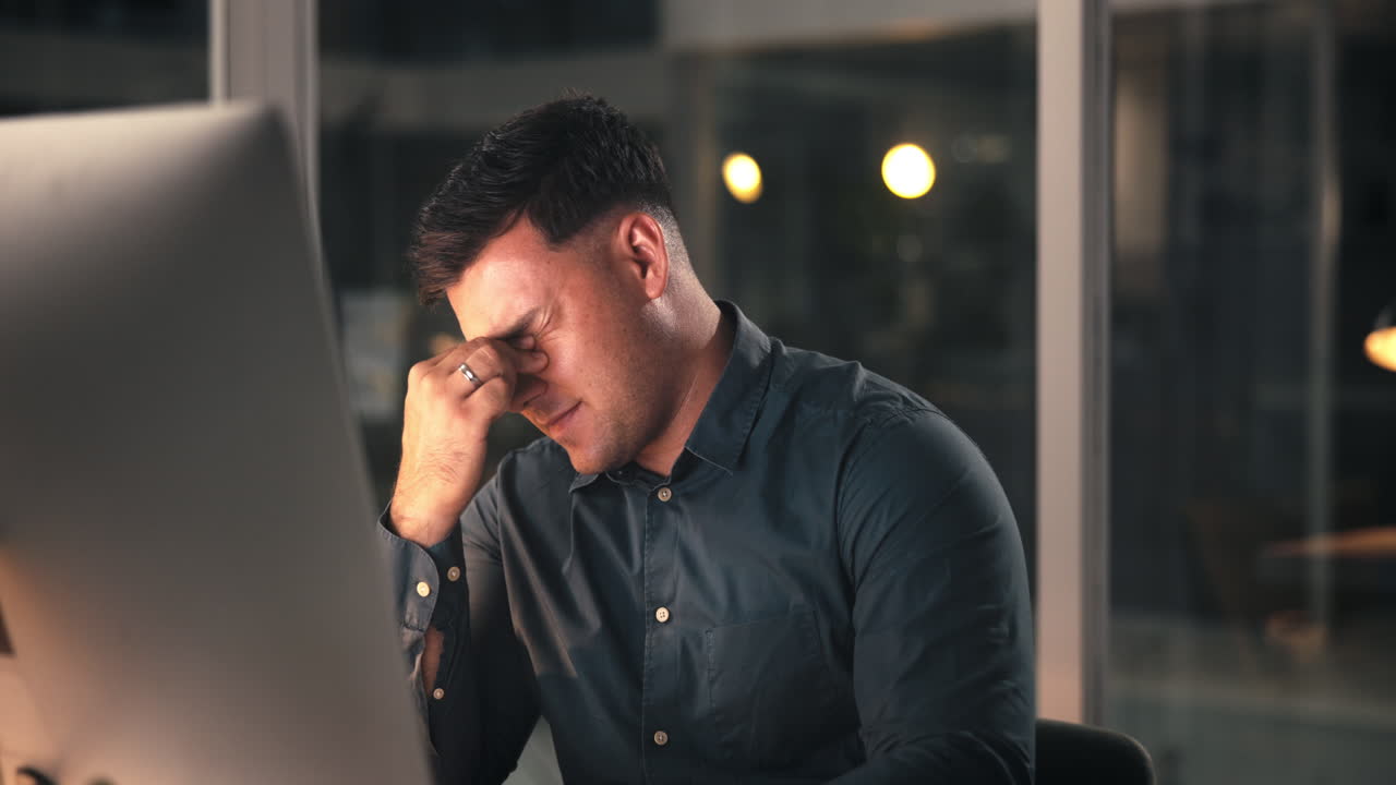 Hombre cansado frotándose los ojos mientras trabaja en el ordenador por la noche