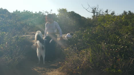 girl sitting on a rock surrounded by vegetation bush and being greeted by pet mongrel dog